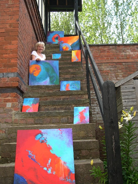 Stella Hidden, artist, with some of her colourful colorful acrylic abstract expressionist non-representational paintings on the 
	steps of her Herefordshire Dovecote studio